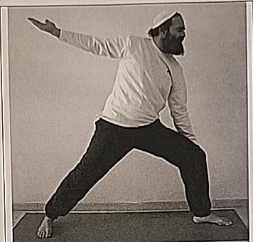 Photograph of a practitioner performing the Aleph posture, inside view, facing left, in a wide lunge with arms extended.