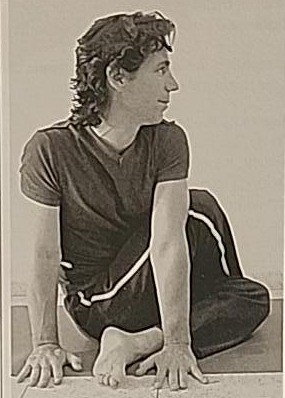 Photograph of a practitioner performing the Ayin twist, right view, hands planted on the floor beside the foot.