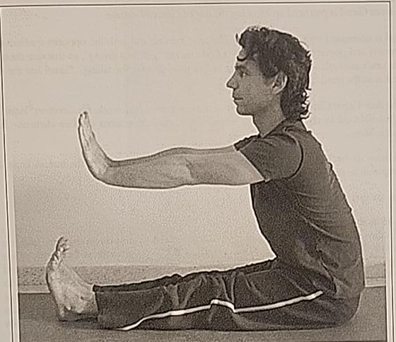 Photograph of a practitioner performing the Bet posture, seated with legs extended and arms reaching toward the feet.