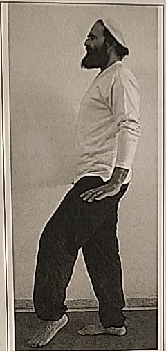 Photograph of a practitioner performing the Gimel posture, standing with one heel lifted as if suspended mid-step.
