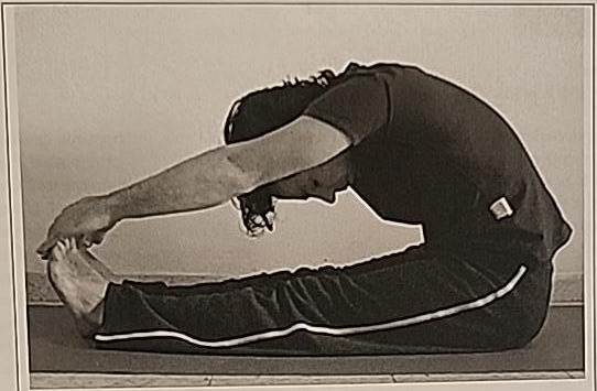 Photograph of a practitioner performing the Khaf posture, folded forward over extended legs, reaching for the toes with head toward the knees.