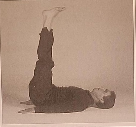 Photograph of a practitioner performing the Final Khaf posture, lying on the back with legs raised straight up at a 90 degree angle.