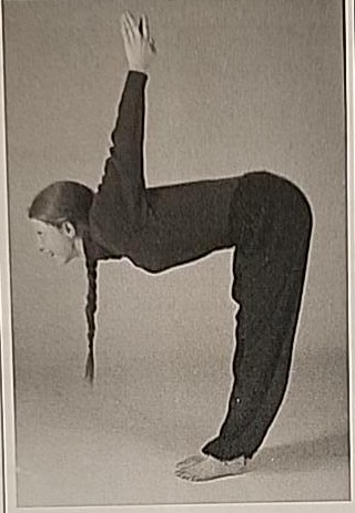 Photograph of a practitioner performing the Lamed posture, bent forward at a right angle with arms raised behind the back, palms pressed together.