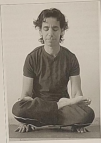 Photograph of a practitioner performing the Flying Mem posture, cross-legged with hands on the ground and legs lifted.