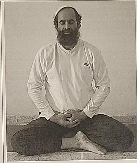 Photograph of a practitioner sitting cross-legged in the Mem posture, hands resting together at the navel.