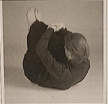 Photograph of a practitioner performing the Final Mem posture, curled on the back hugging the knees to the chest.