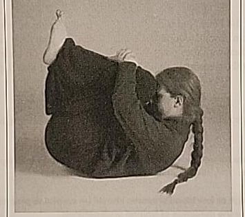 Photograph of a practitioner performing the Final Mem posture from a second angle, curled forward with forehead toward the knees.