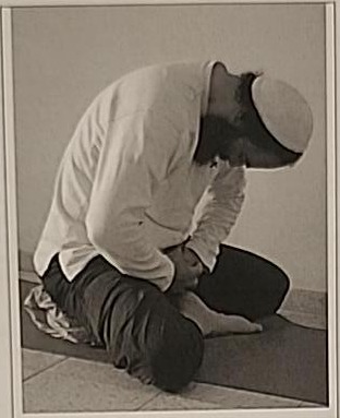 Photograph of a practitioner performing the Peh posture, folded forward with head resting down toward the lap, cross-legged.
