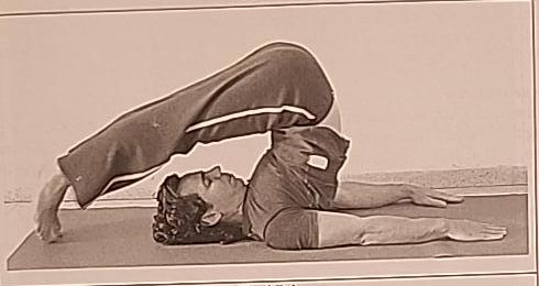Photograph of a practitioner performing the Final Peh posture, a plow-like pose lying on the back with legs extended overhead and toes touching the floor.
