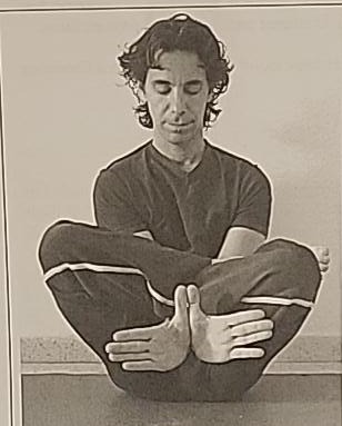 Photograph of a practitioner performing the intermediate Samech position, seated cross-legged with hands pressing down between the legs.