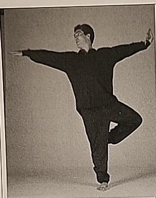 Photograph of a practitioner performing Shin Variation #3, balancing on the right leg with the right arm extended palm-down and the left arm bent with palm facing the face, head turned right.