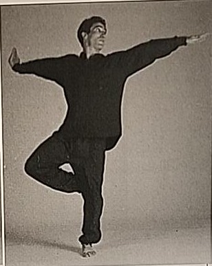 Photograph of a practitioner performing Shin Variation #4, the mirrored pose balancing on the left leg with arm positions reversed and head turned left.