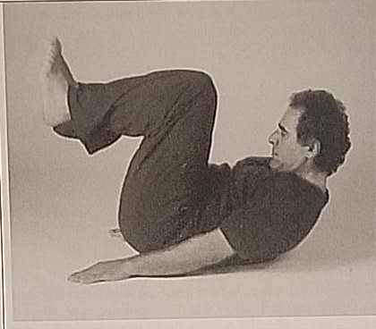 Photograph of a practitioner performing the Tet posture, lying on the back with knees bent toward the chest and palms flat on the floor.