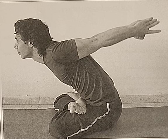 Photograph of a practitioner performing the Tzadi posture, seated cross-legged and bent forward with arms raised behind the back.