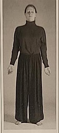 Photograph of a practitioner performing the Vav posture, standing relaxed with arms hanging at the sides.