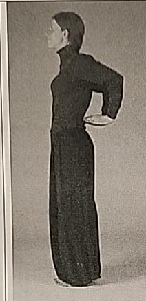 Photograph of a practitioner performing the Zayin posture from the side, arms bent behind the back.